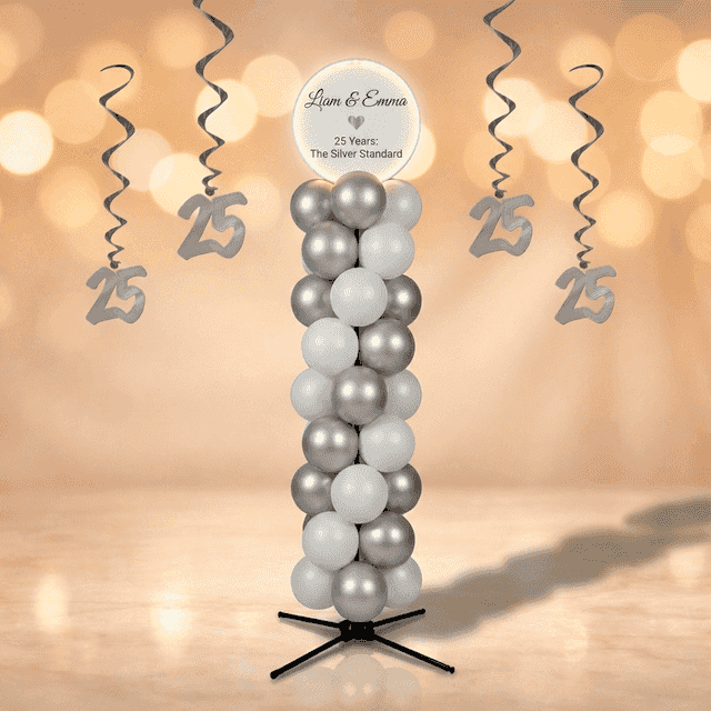 Columna de globos plateada y blanca con panel superior circular blanco con nombres de aniversario, en un salón de fiestas champán dorado con lámparas de cristal