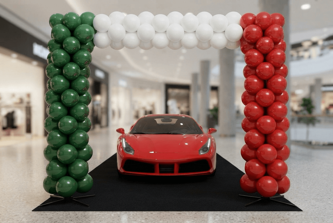 Columnas de globos en verde, blanco y rojo con un arco encima, alrededor de un deportivo rojo en el showroom