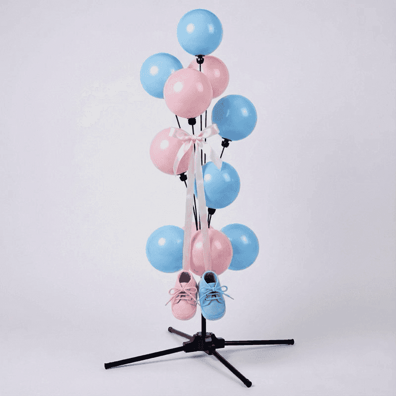 Tierna fuente de globos gender reveal con patucos de bebé rosa y azul colgando de cintas doradas entre los globos
