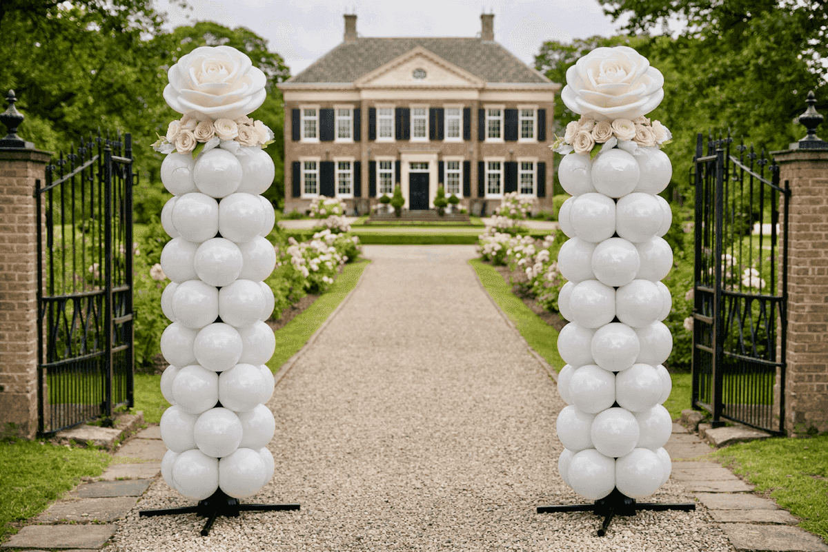 Dos columnas de globos blancos con flores rosas en la entrada de una finca